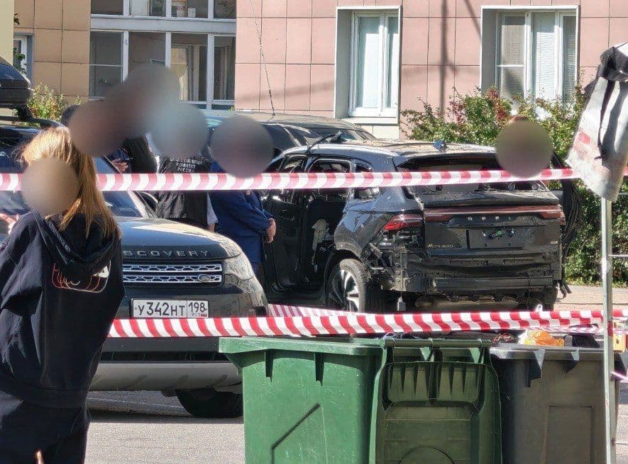 Пошкоджений чорний автомобіль на вулиці, поруч люди та розкидані уламки.