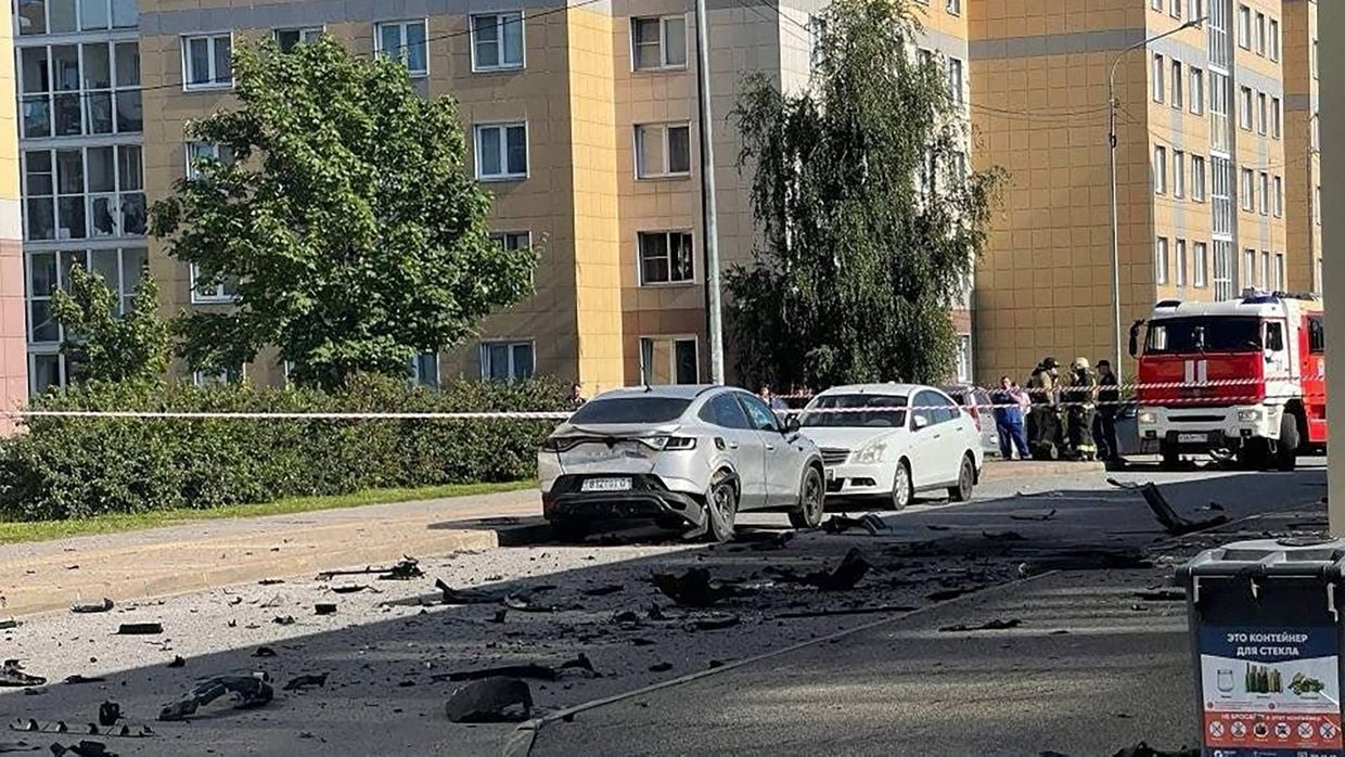 Дві машини біля житлового будинку, навколо уламки та працюють рятувальники.